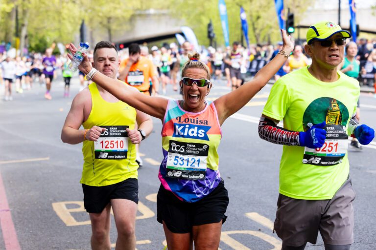a woman in a Kids vest is running with both hands up in the air