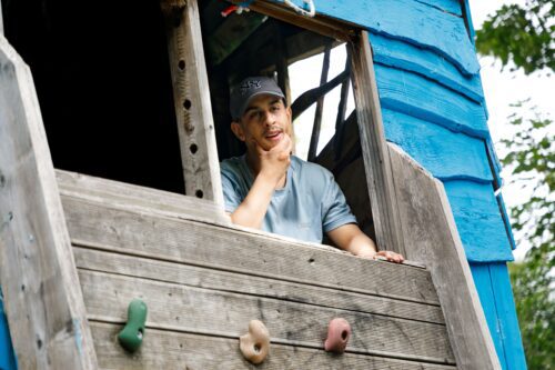 A young person is looking out a cabin playhouse, one hand on his chin