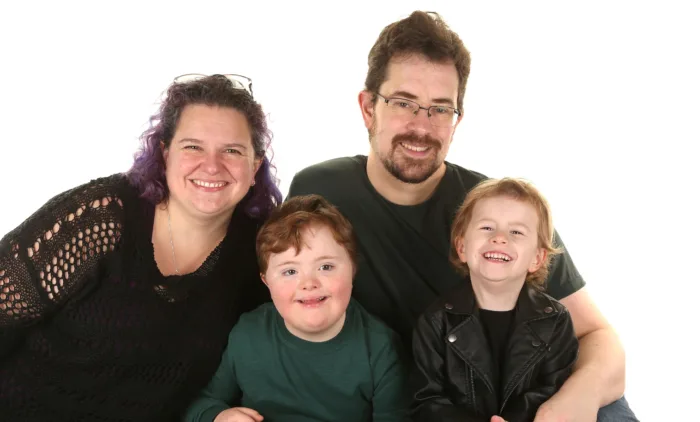 A family of four photographed together. There is a white background behind them