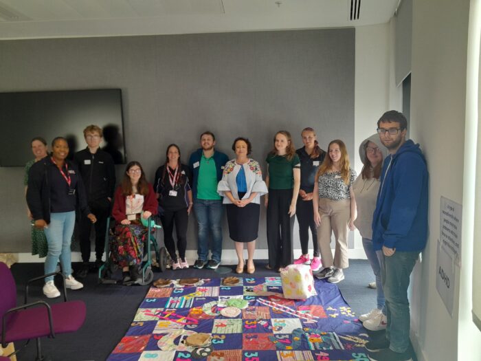 a group of young people are standing and smiling, in front of them is a giant snakes and ladders game