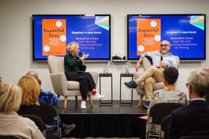 cathy newman and stephen unwin sitting in armchairs opposite each other talking in front of a crowd of people