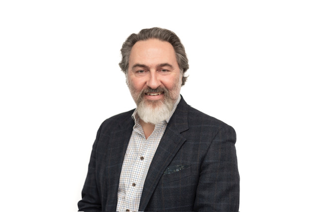 Mark is pictured against a white background wearing a grey suit jacket and white shirt