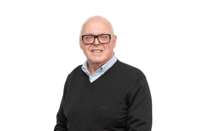 Richard is pictured against a white background wearing a black jumper and glasses
