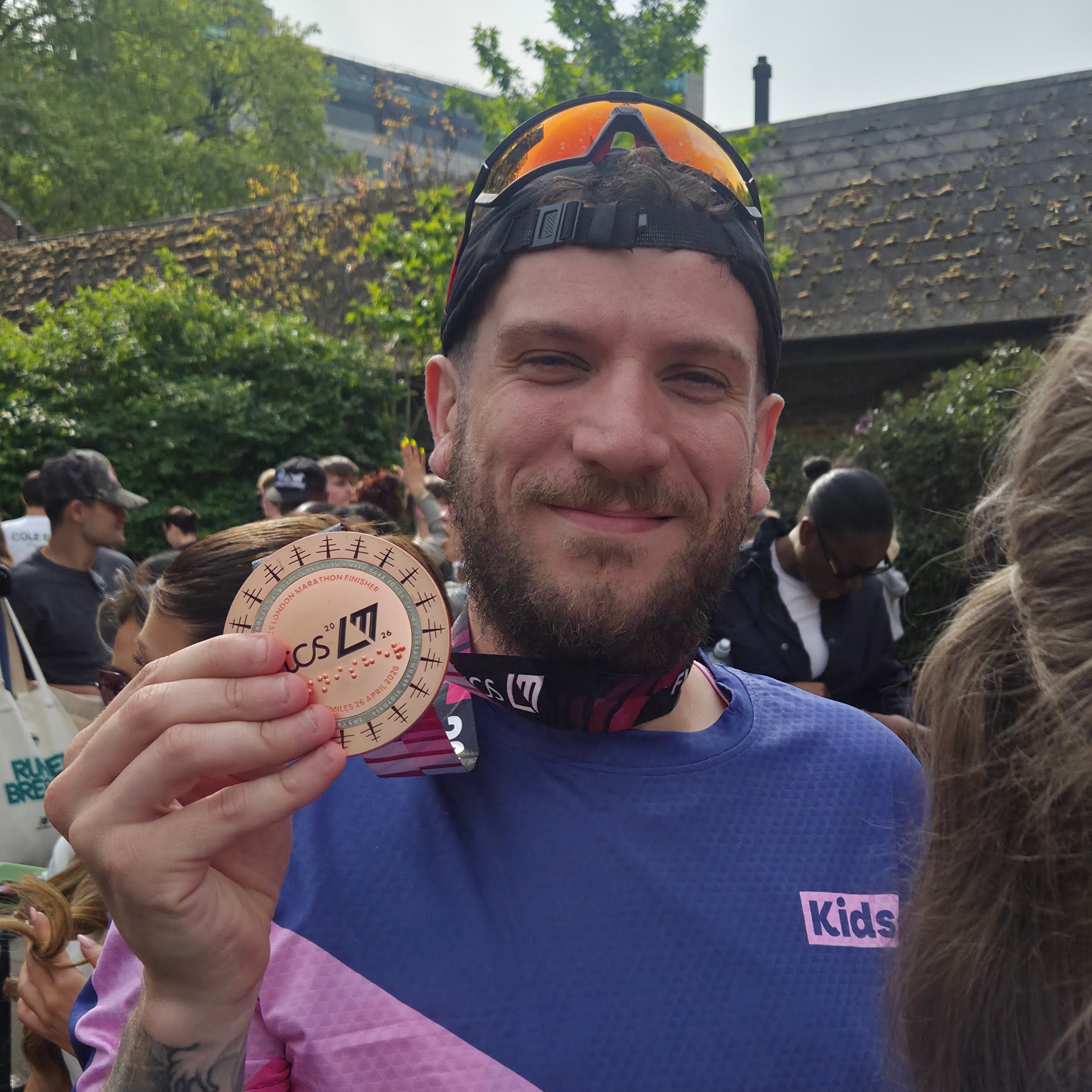 man smiles whilst holding his medal wearing a Kids running vest